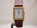 Front view of the Raymond Weil 5722 watch with a white rectangular dial, black Arabic numerals, and gold hands, on a brown leather strap.