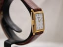 Opposite angled side profile of the Raymond Weil watch on a display stand, highlighting the rectangular gold case and textured brown strap.