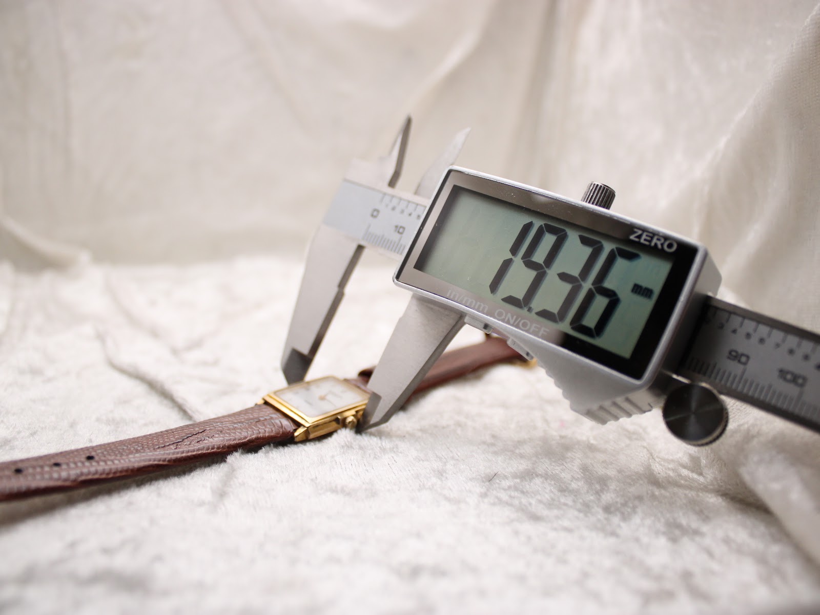 Digital caliper measuring the width of the Raymond Weil watch case from the side, displaying an exact measurement of 19.36 mm.