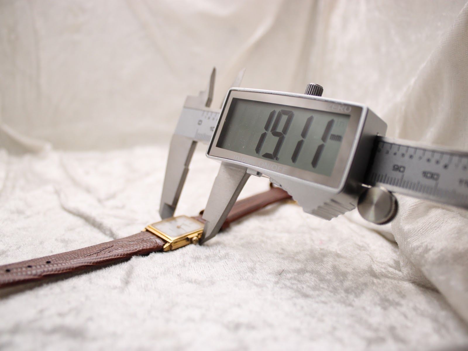 Digital caliper measuring the width of the Raymond Weil watch case from a different angle, displaying an exact measurement of 19.11 mm.
