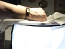 A person's wrist wearing the rectangular Raymond Weil watch, with the watch dial partially visible against a bright, soft background.