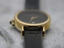 Side view close-up of the gold-plated watch case and lugs, with part of the black leather strap visible.