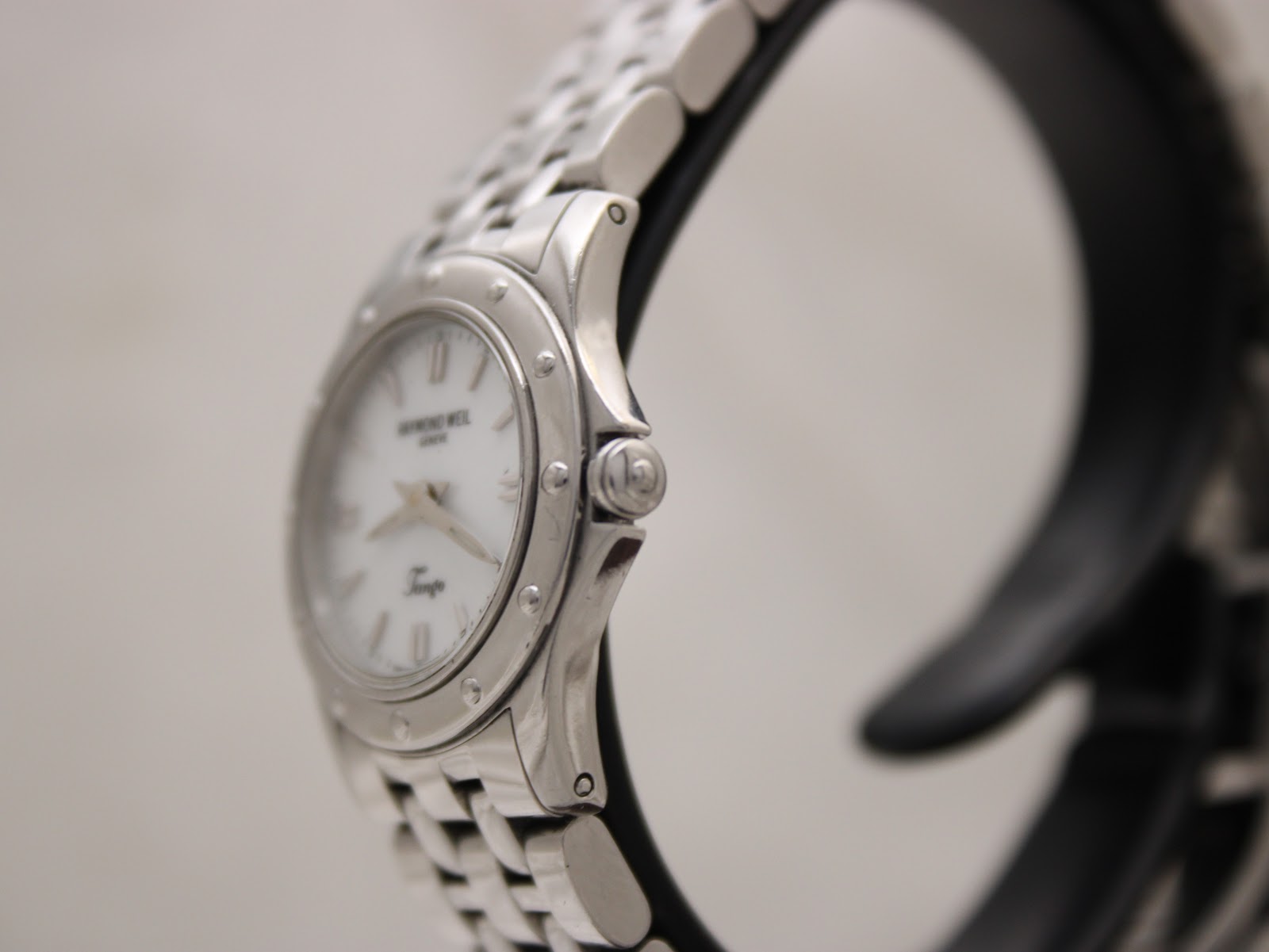 Angled side view of the Raymond Weil Tango 5790 watch, highlighting the polished bezel, crown, and the curved profile of the stainless steel case and bracelet.