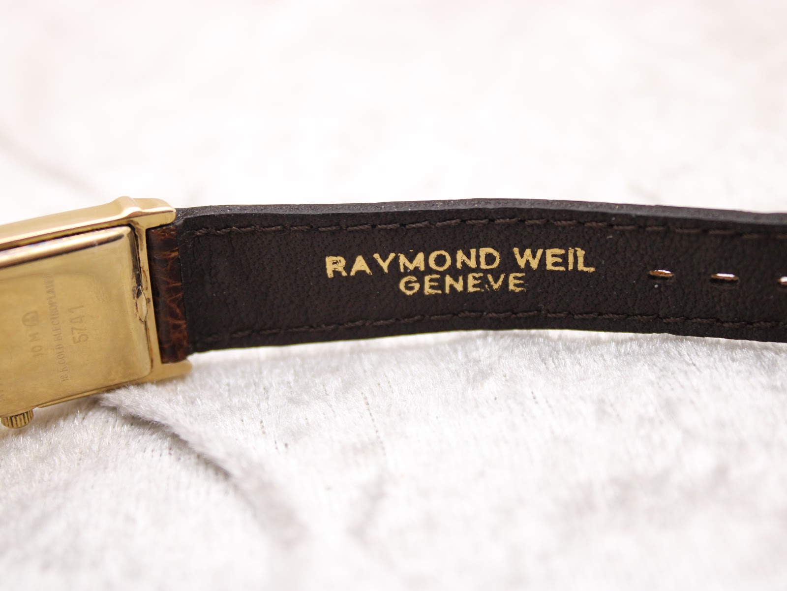 Close-up of the underside of the brown crocodile leather strap showing "RAYMOND WEIL GENEVE" embossing