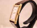 Side profile view of the Raymond Weil watch on a display stand, showing the gold case and crown