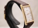 Three-quarter view of the Raymond Weil watch on a display stand, highlighting the rectangular gold case and brown strap