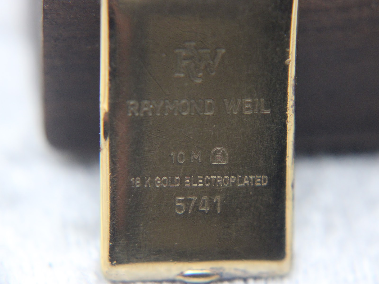 Close-up of the watch case back showing "RW", "RAYMOND WEIL", "10 M", "18 K GOLD ELECTROPLATED", and "5741" engravings