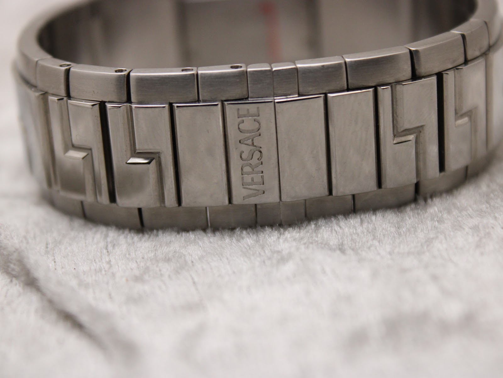 Close-up of the bracelet showing 'VERSACE' engraved on a link and the distinctive greca pattern.