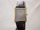 Front view of the gold-tone Seiko quartz watch with a grey dial and dark brown leather strap, on a white background.