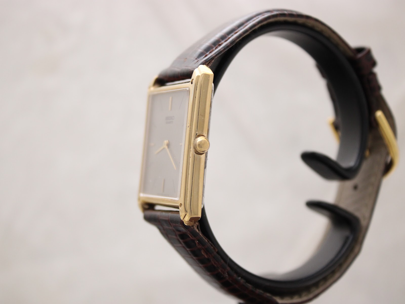 Side profile view of the gold-tone rectangular Seiko watch on a display stand, showing the crown on the right.