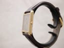 Side profile view of the gold-tone rectangular Seiko watch on a display stand, showing the crown on the right.