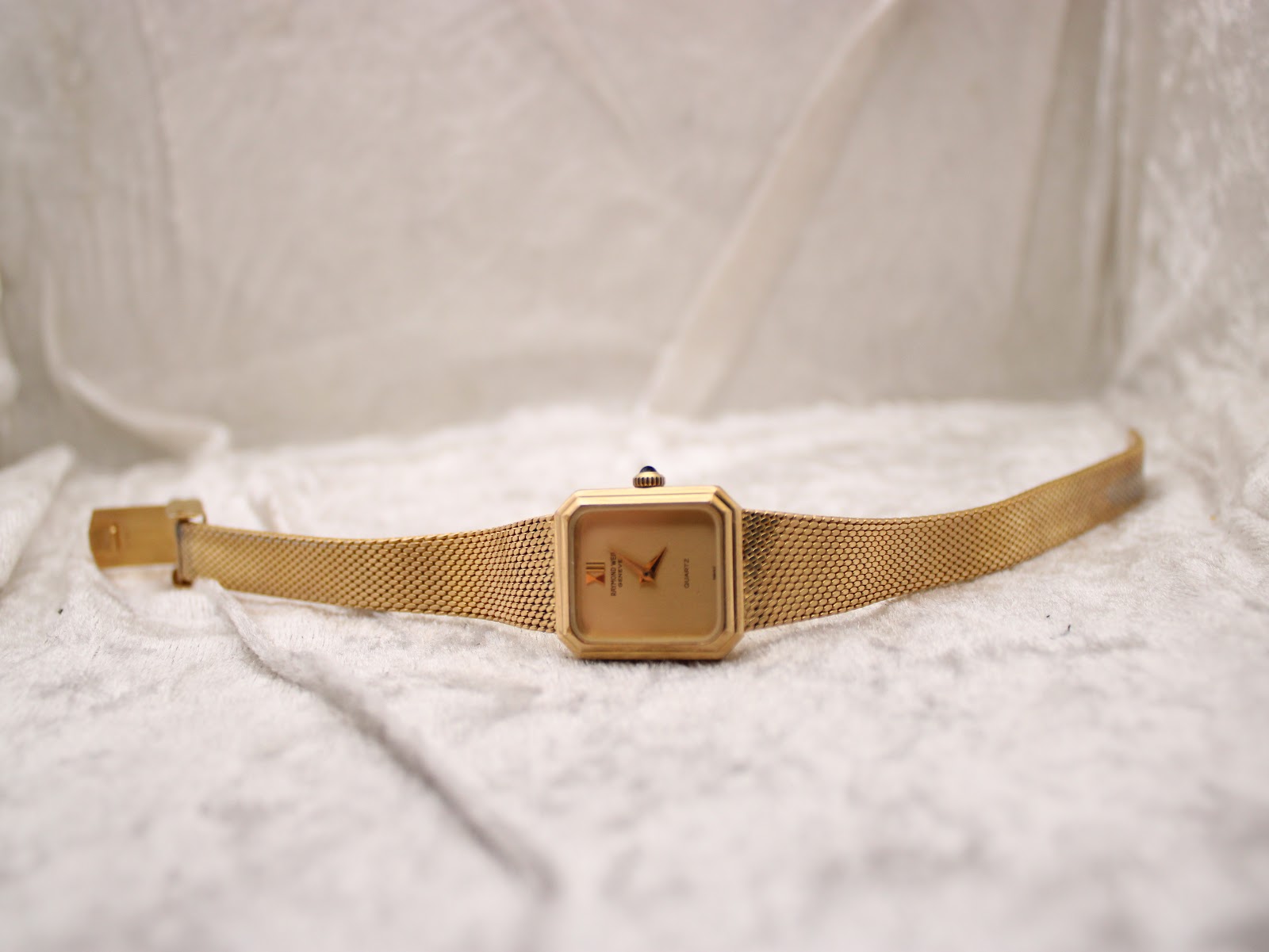 Top-down view of the watch on a white textured surface, showcasing the dial and integrated bracelet fully extended.