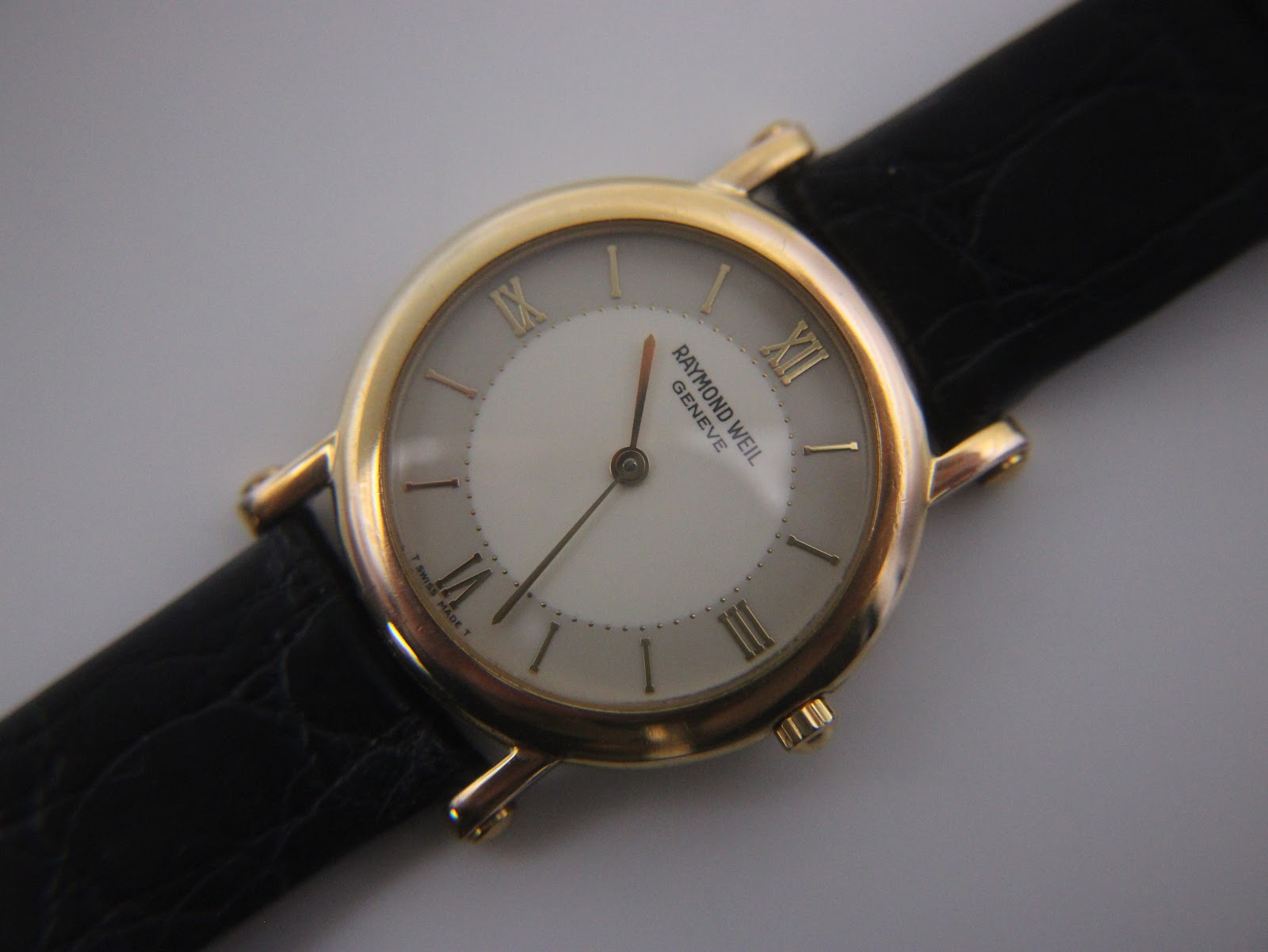 Close-up of the cream dial of the Raymond Weil watch, showing Roman numerals, baton indices, and gold-tone hands.