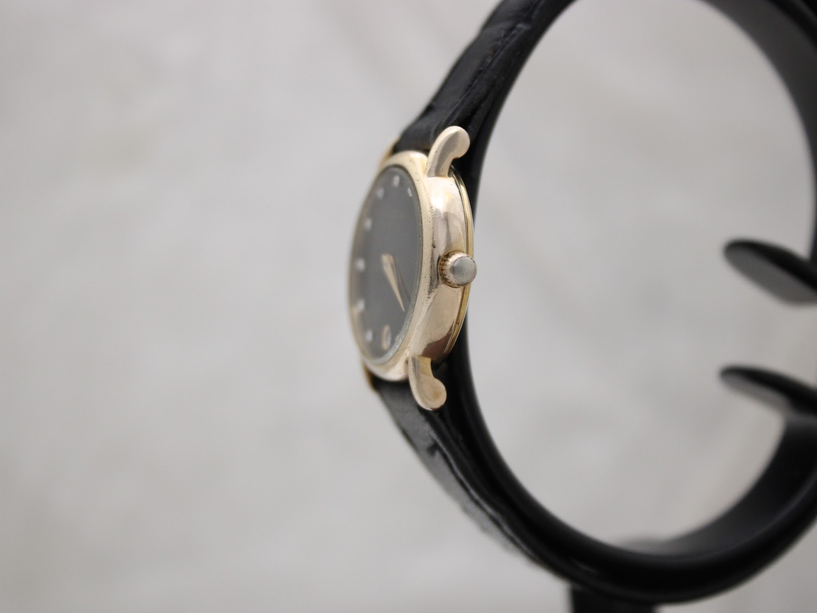 Side view of the Raymond Weil 9923 watch on a stand, showing the gold case and crown.
