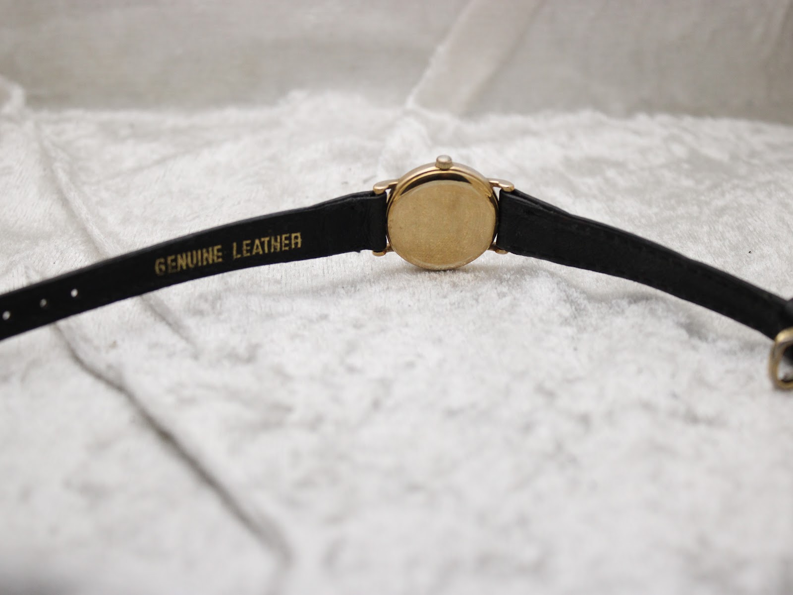 View of the watch from the back, showing the 'Genuine Leather' embossed strap and the gold-tone case back.