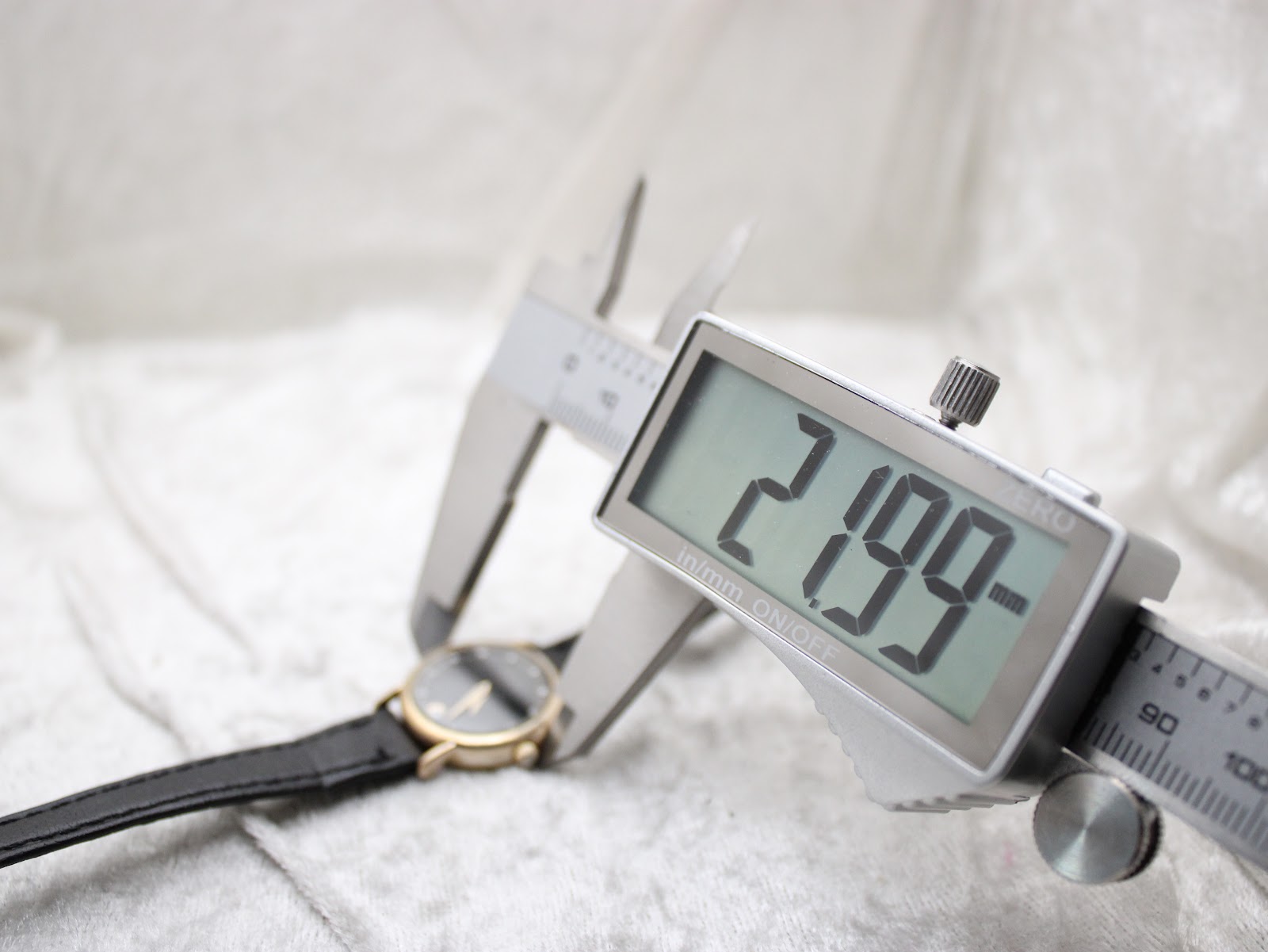 Digital caliper measuring the watch case, displaying a precise diameter of 21.99 mm.