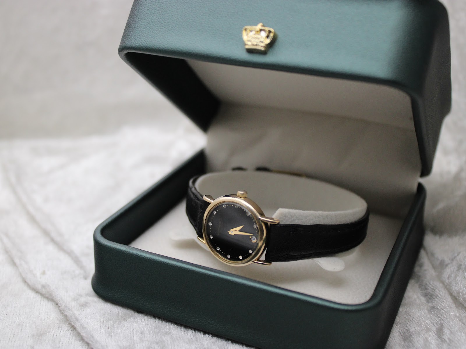 Raymond Weil watch displayed inside a deep green watch box with a gold crown emblem on the lid.