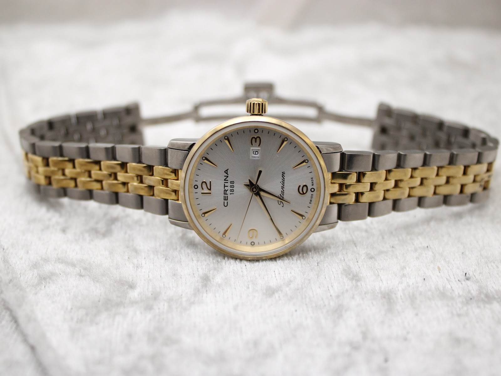 Full front view of the Certina DS Caimano watch with its two-tone bracelet laid flat on a light textured surface, clasp open.