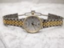Full front view of the Certina DS Caimano watch with its two-tone bracelet laid flat on a light textured surface, clasp open.