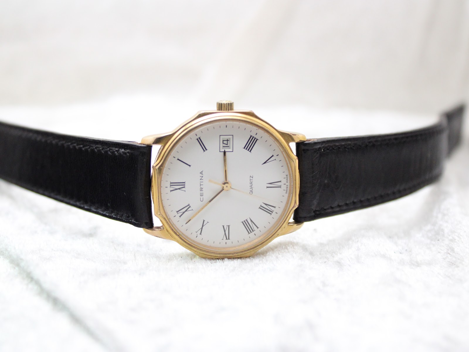 Full front view of the Certina watch with its black leather strap laid flat on a white textured surface.