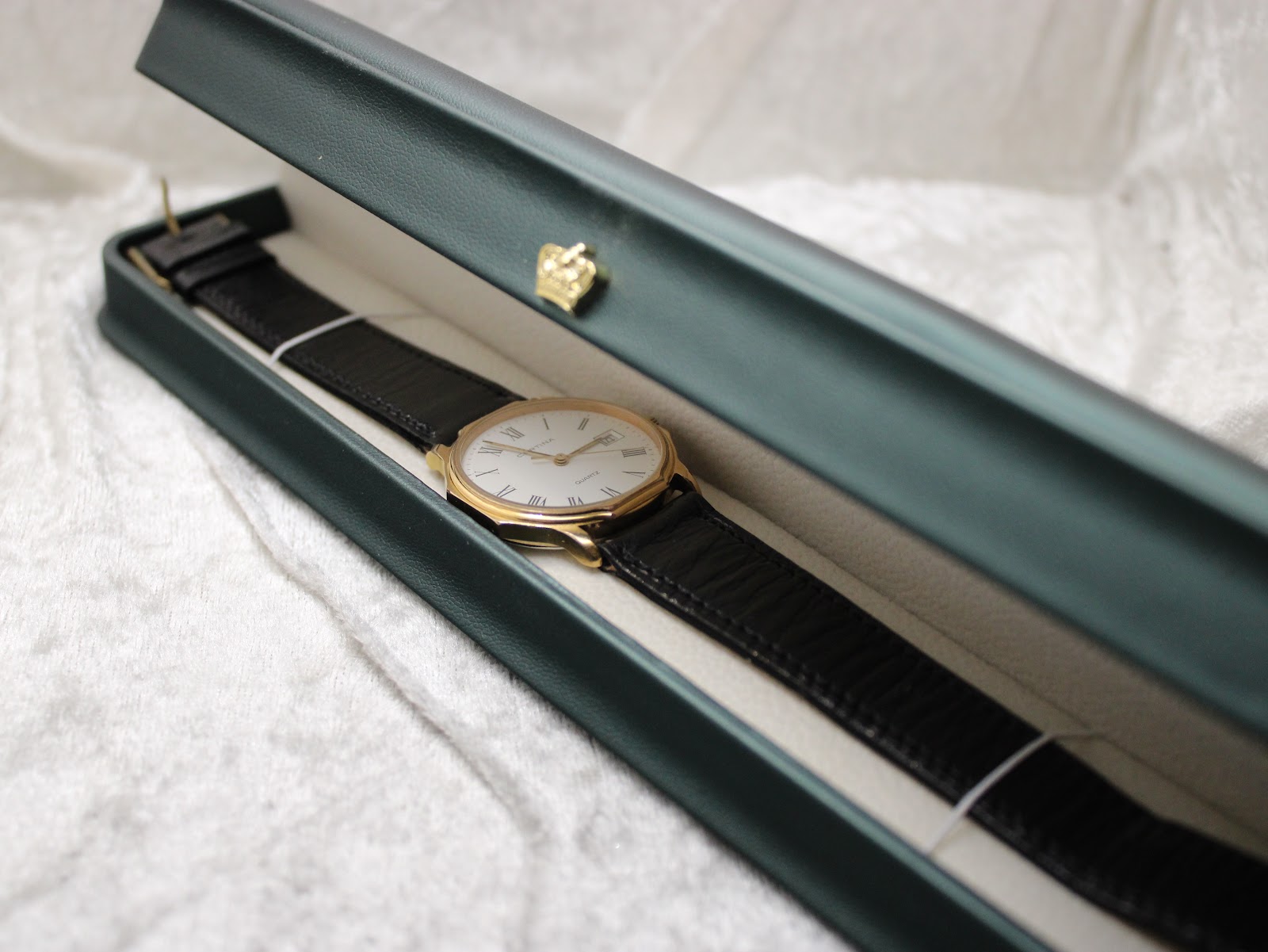 Certina watch with black strap placed inside a green hinged presentation box.