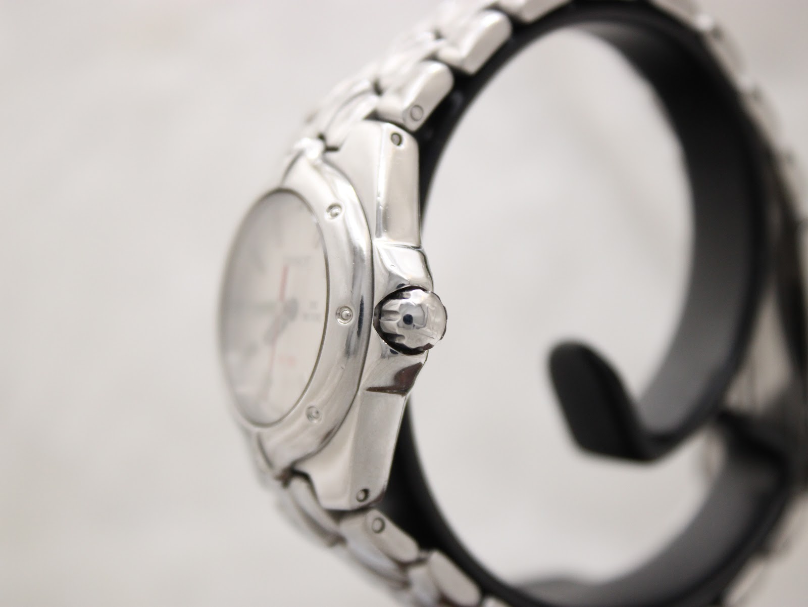 Side view of the Tissot PR 200 watch on a stand, highlighting the signed "T" crown and curved stainless steel case.
