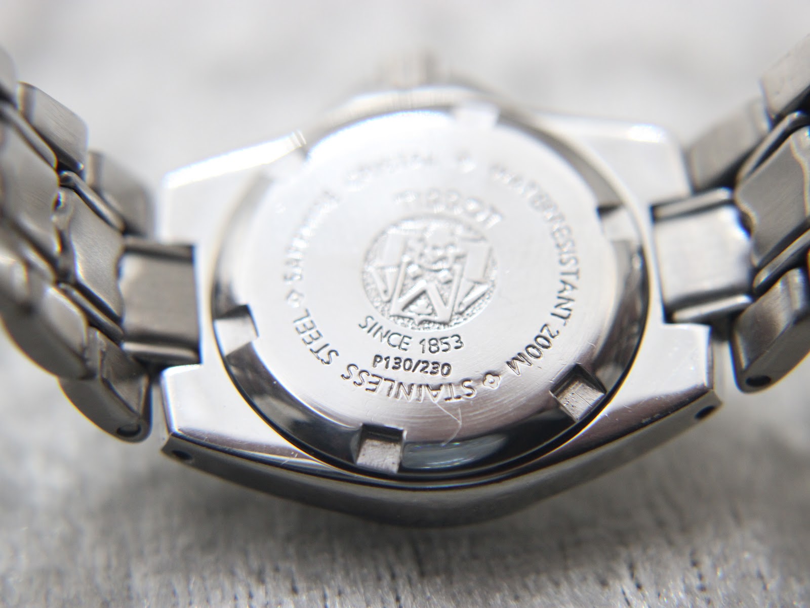 Close-up of the screw-down stainless steel case back, engraved with Tissot emblem, "Since 1853", "P130/230", "Stainless Steel", "Sapphire Crystal", and "Water Resistant 200M".