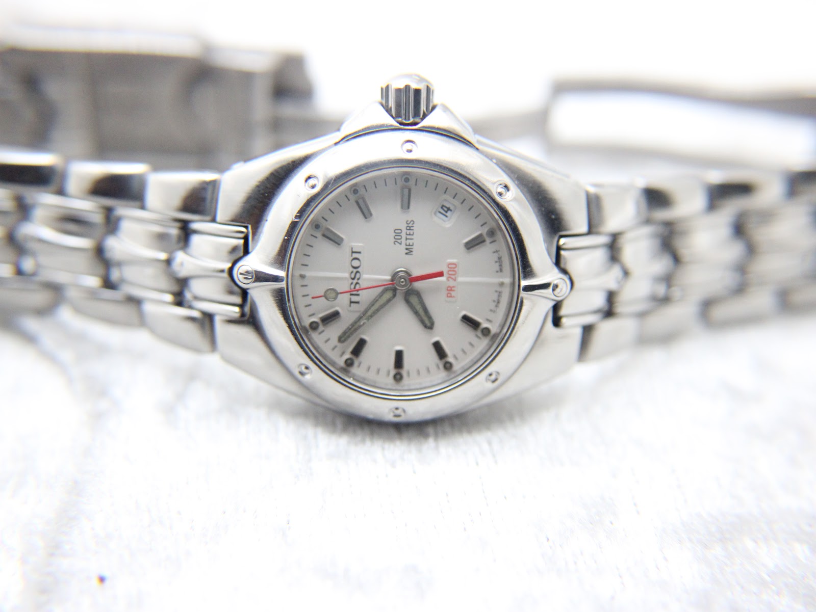 Front oblique view of the Tissot PR 200 watch and its integrated stainless steel bracelet, showing the dial and date window.