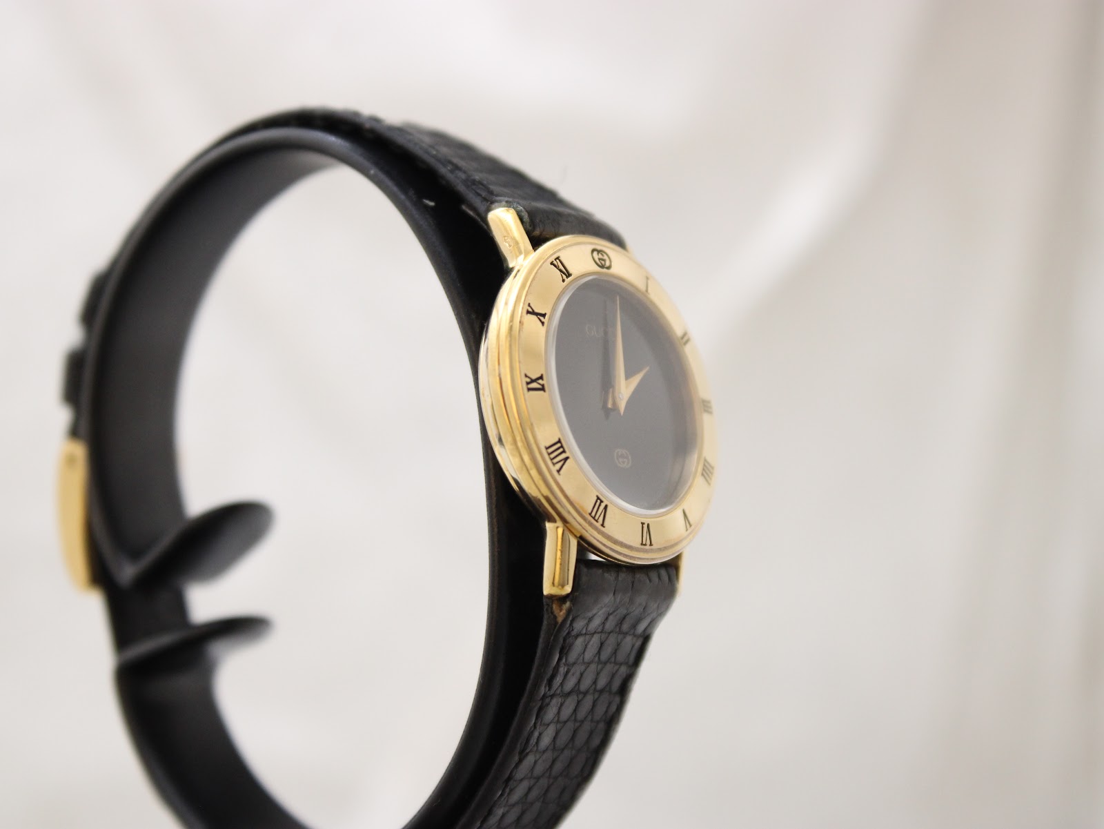 Close-up of signed Gucci gold buckle on black leather strap.