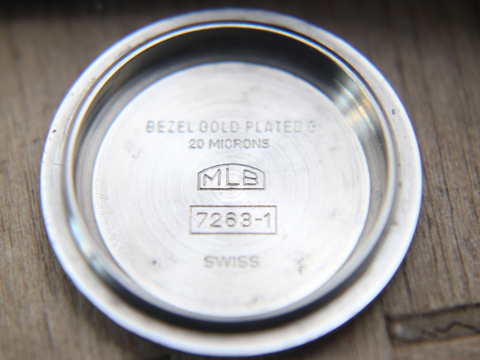 Close-up of the inside of the stainless steel case back, engraved with "BEZEL GOLD PLATED B 20 MICRONS", "MLB", "7263-1", and "SWISS".