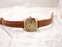 Full view of the Bulova watch with its brown leather strap laid flat on a white textured surface.