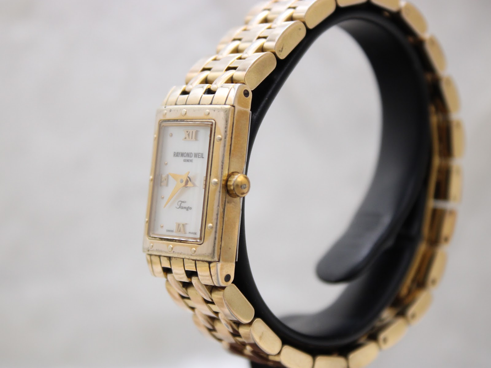 Right side view of the Raymond Weil Tango watch on a black display stand, showing the fluted crown.