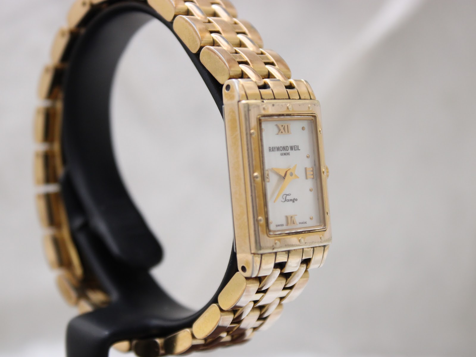 Left side view of the Raymond Weil Tango watch on a black display stand.
