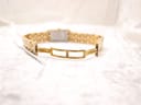 View of the gold-tone double-fold clasp and bracelet opened flat on a white textured surface.
