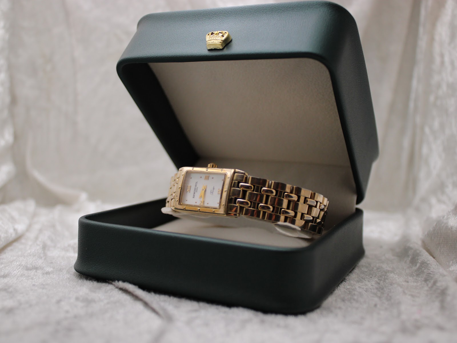 The Raymond Weil Tango watch presented inside an open dark green watch box with a gold crown emblem.