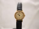 Front view of the Raymond Weil ladies' watch, gold-plated case, cream dial with Roman numerals, black leather strap, on a watch stand.
