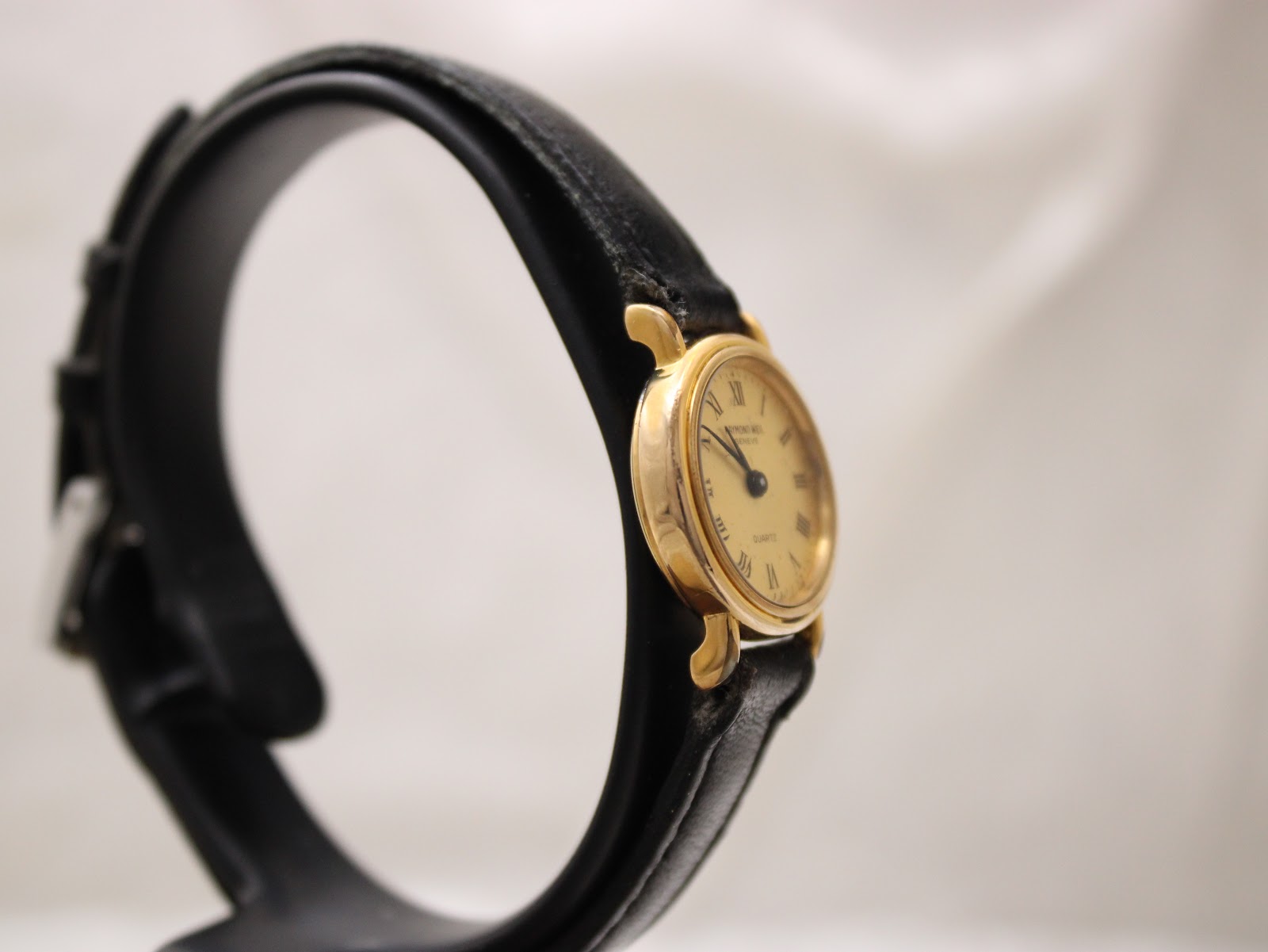 Angled side view of the watch on a stand, highlighting the thin profile of the gold-plated case and black leather strap.