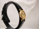 Angled side view of the watch on a stand, highlighting the thin profile of the gold-plated case and black leather strap.