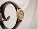 Angled side view of the Raymond Weil 683 watch on a stand, showing the curved gold-tone case and part of the brown leather strap.