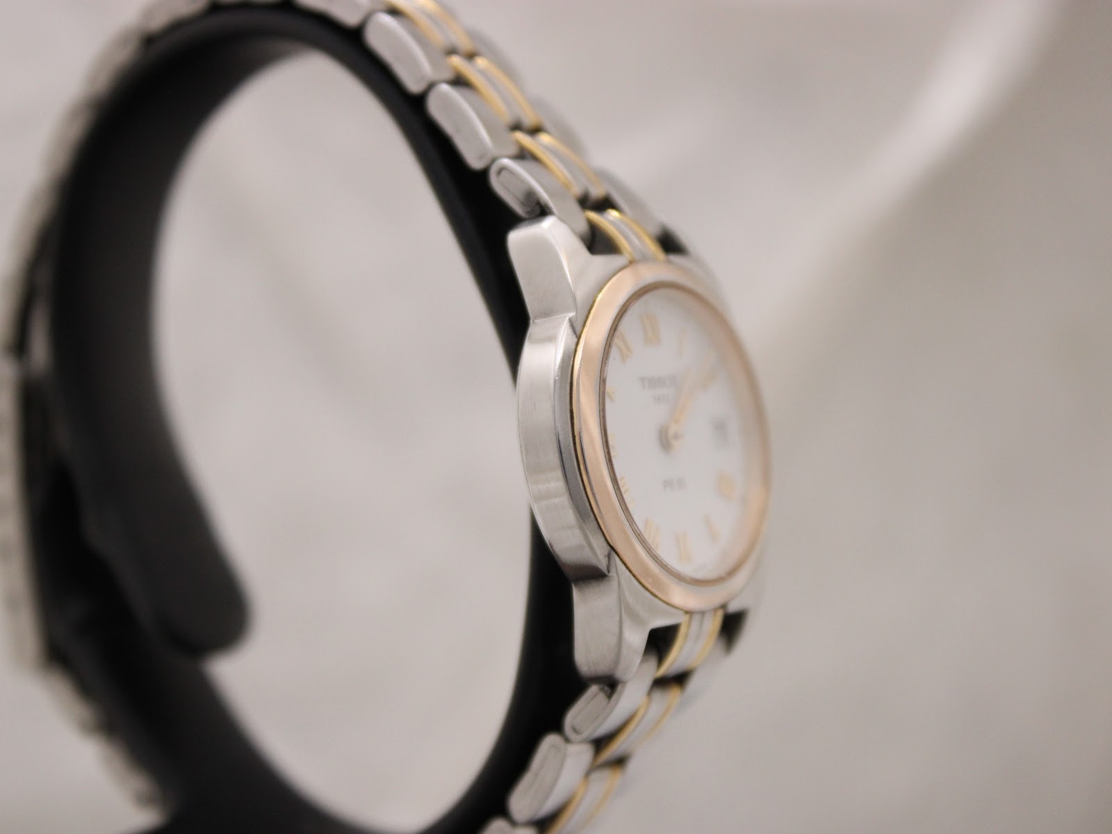 Angled side view of the Tissot PR 50 watch, highlighting the stainless steel case and gold-tone bezel.