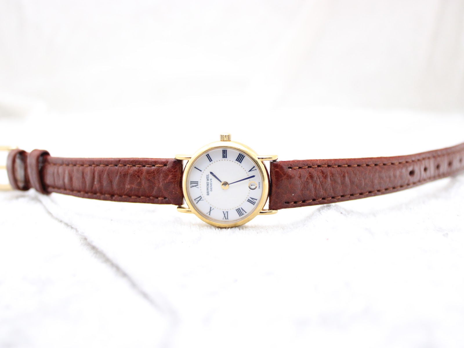 Top-down view of the Raymond Weil 9923 watch laid flat, displaying the white Roman numeral dial and extended brown leather strap.