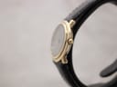 Side view of the gold electroplated watch case and fluted crown, showing its slim profile on a black leather strap.
