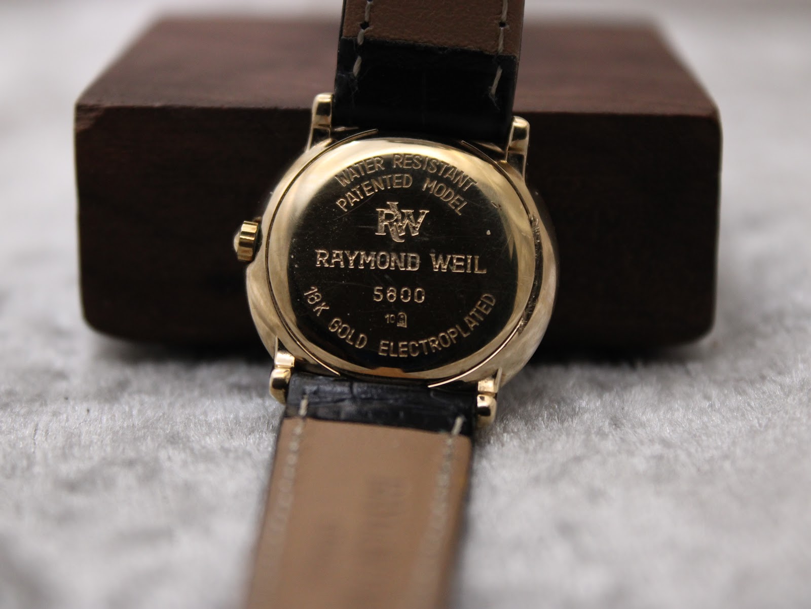 Close-up of the watch case back, engraved with 'Raymond Weil', '5800', '18K Gold Electroplated', and 'Water Resistant Patented Model'.