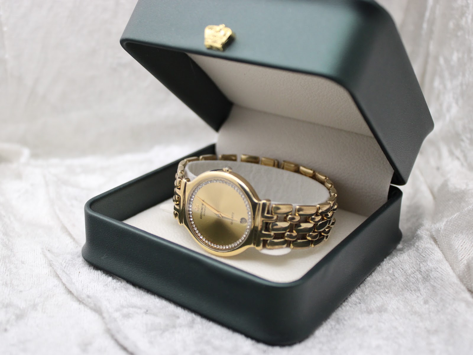 The Raymond Weil watch presented inside a dark green watch box, highlighting its gold aesthetic.