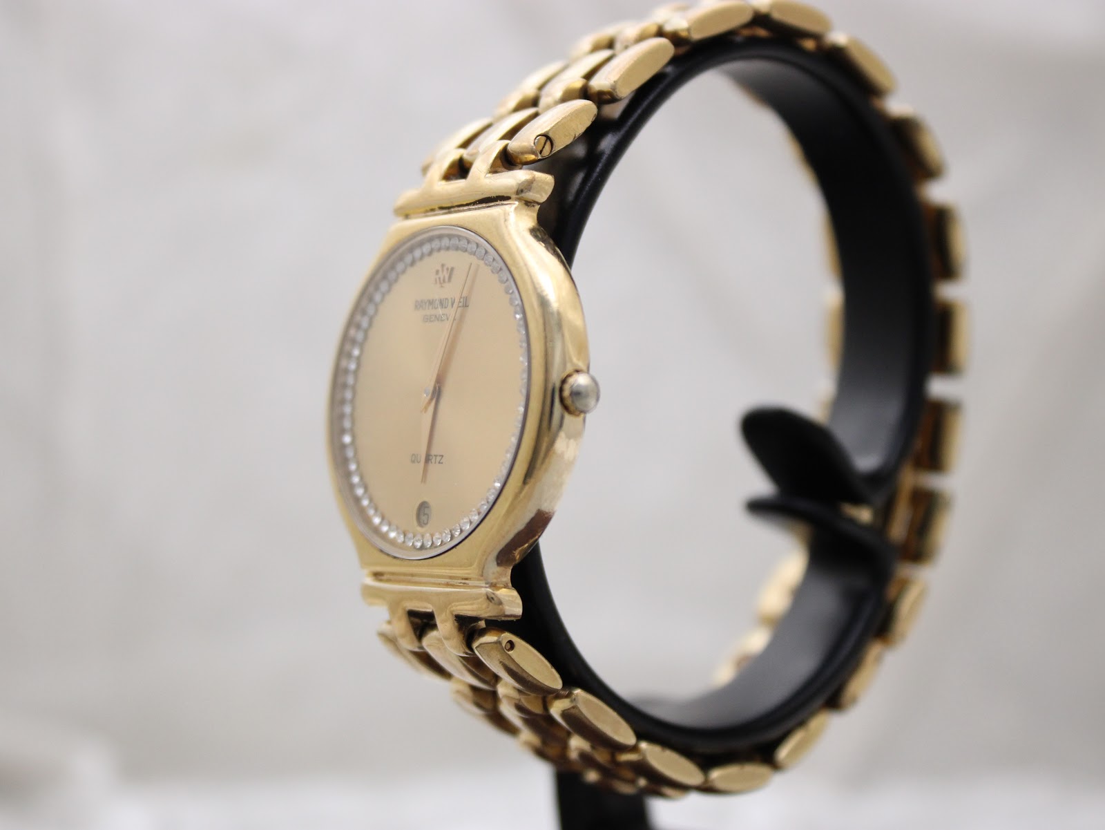 Side view of the gold-tone Raymond Weil watch displayed on a watch stand, showing its slim profile and small crown.