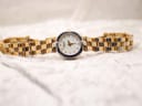 Full Raymond Weil watch laid flat on a white textured surface, showcasing the two-tone bracelet