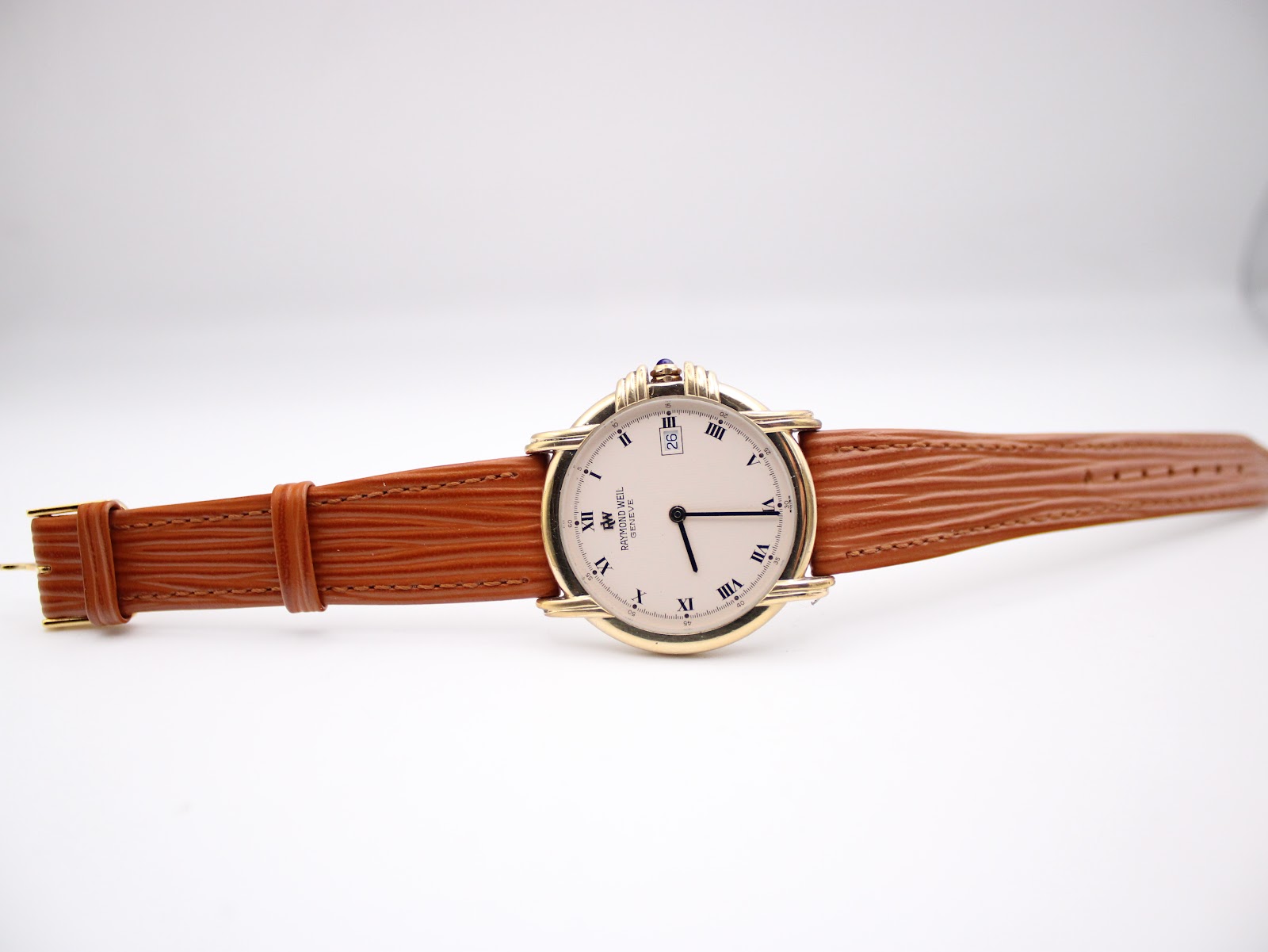 Top-down view of the Raymond Weil 9155 watch with its white roman dial and extended brown leather strap laid flat.