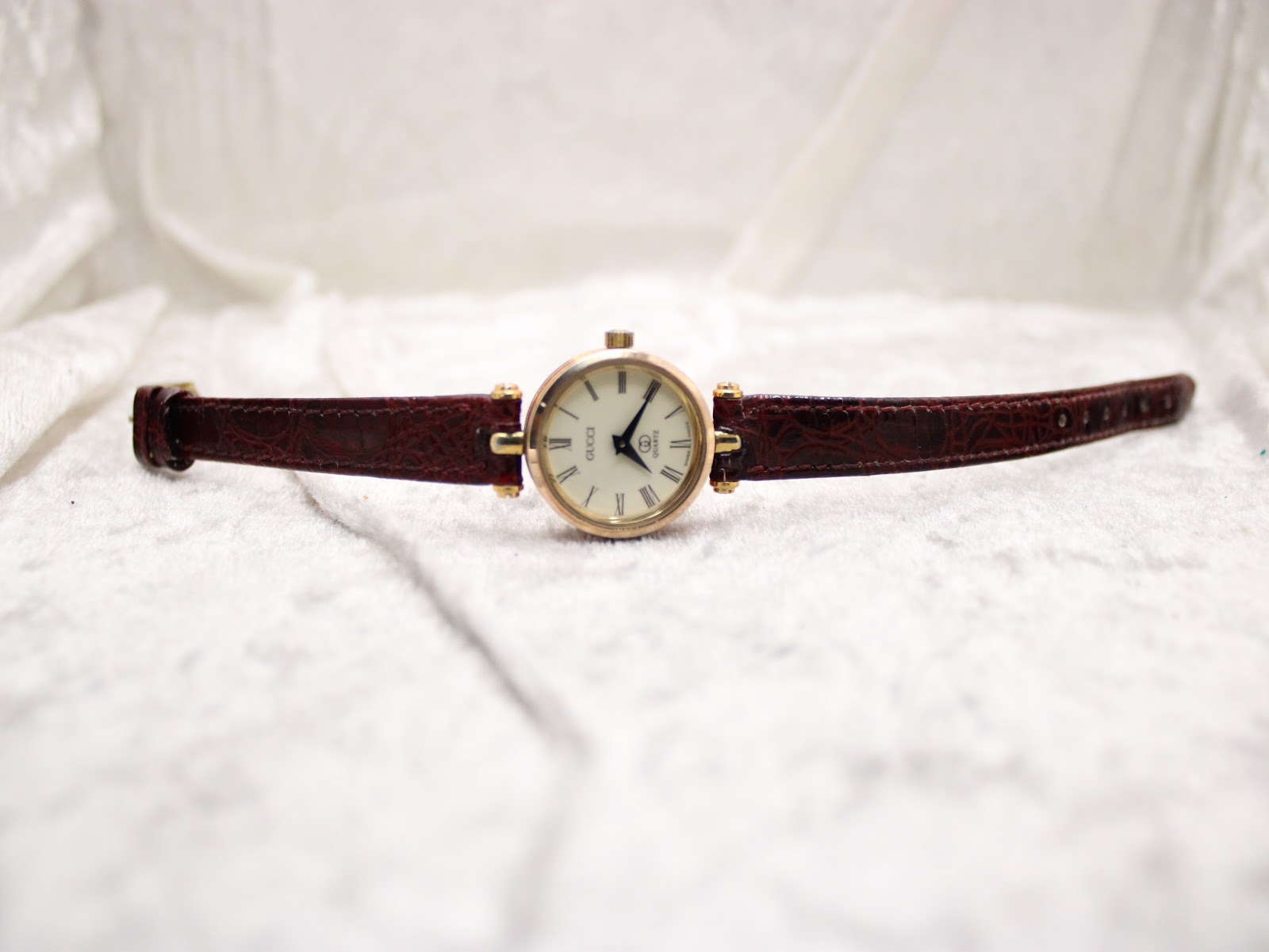 Full front view of the Gucci 2000L watch laid flat on a textured white surface, displaying the burgundy strap.