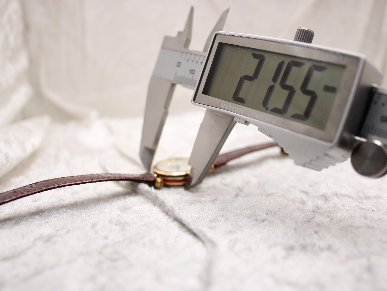 Close-up of a digital caliper measuring the case diameter of the Gucci watch at 21.55 mm.