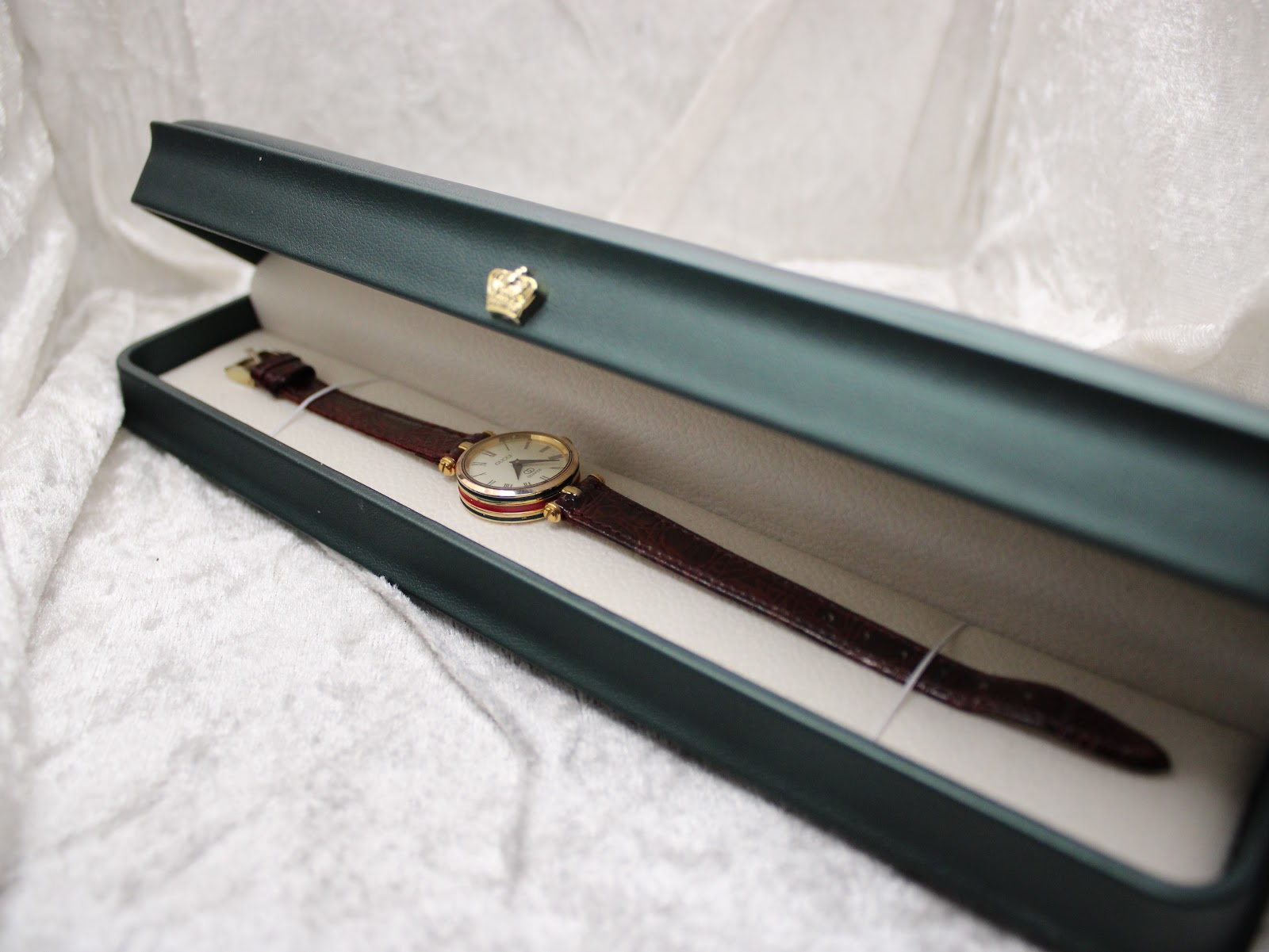 Overhead view of the Gucci 2000L watch nestled inside a dark green watch box with a gold crown emblem.